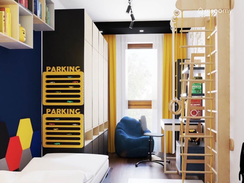 Żółte półki na samochody drewniano czarna szafa niebieska pufa żółte zasłony oraz drewniana drabinka gimnastyczna w pokoju małego chłopca