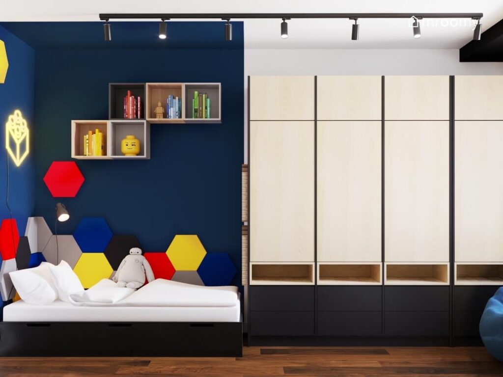 Granatowa strefa spania w pokoju małego chłopca a w niej czarne łóżko kolorowe panele ścienne w kształcie heksagonów i kilka szafek a obok drewniano czarna szafa