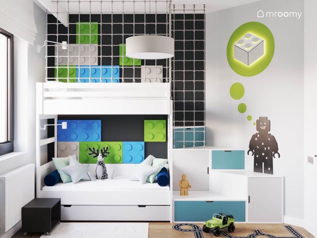 Białe łóżko na antresoli w pokoju chłopca uzupełnione kolorowymi panelami w kształcie klocków pod spodem miejsce do odpoczynku a w schodkach szafki