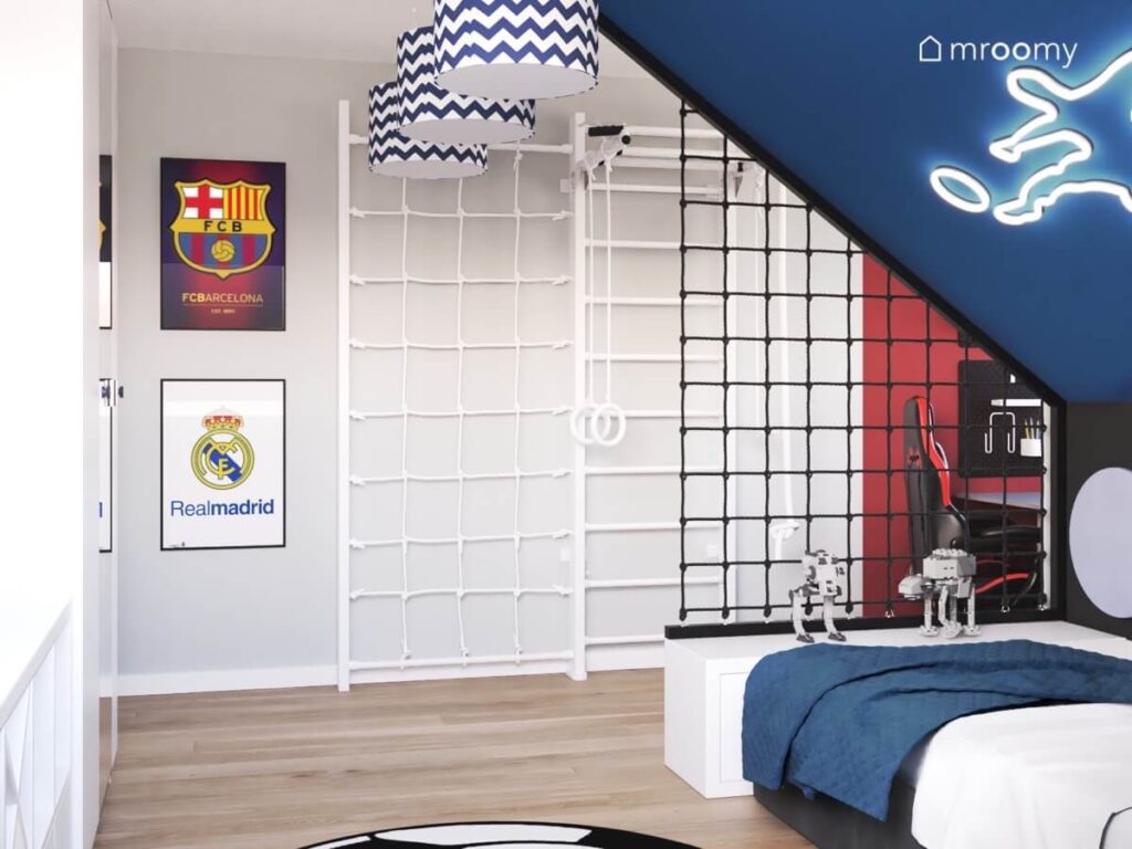 Szaro granatowy pokój dla chłopca miłośnika piłki nożnej a w nim ledon w kształcie piłkarza plakaty z hiszpańskimi klubami futbolowymi oraz drabinka gimnastyczna z siatką