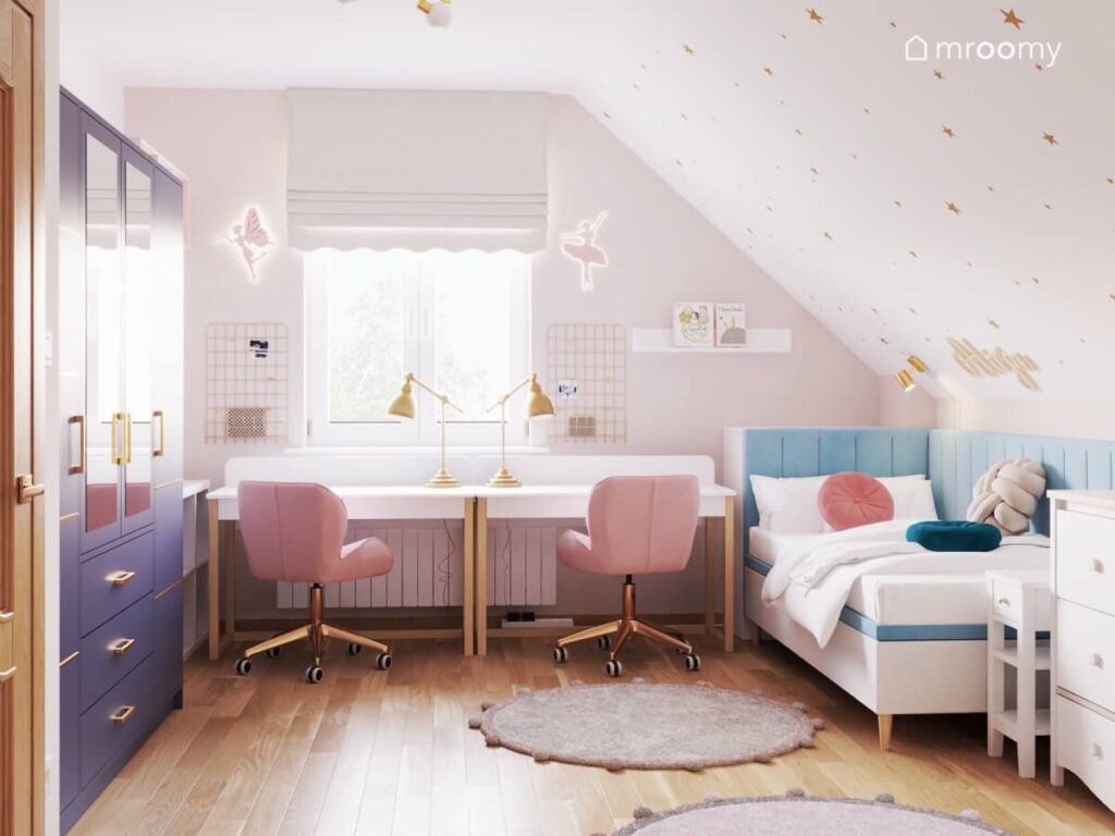Jasny poddaszowy pokój dwóch kilkuletnich dziewczynek a w nim strefa nauki z białymi biurkami i różowymi krzesłami oraz białe łóżka uzupełnione niebieskimi panelami