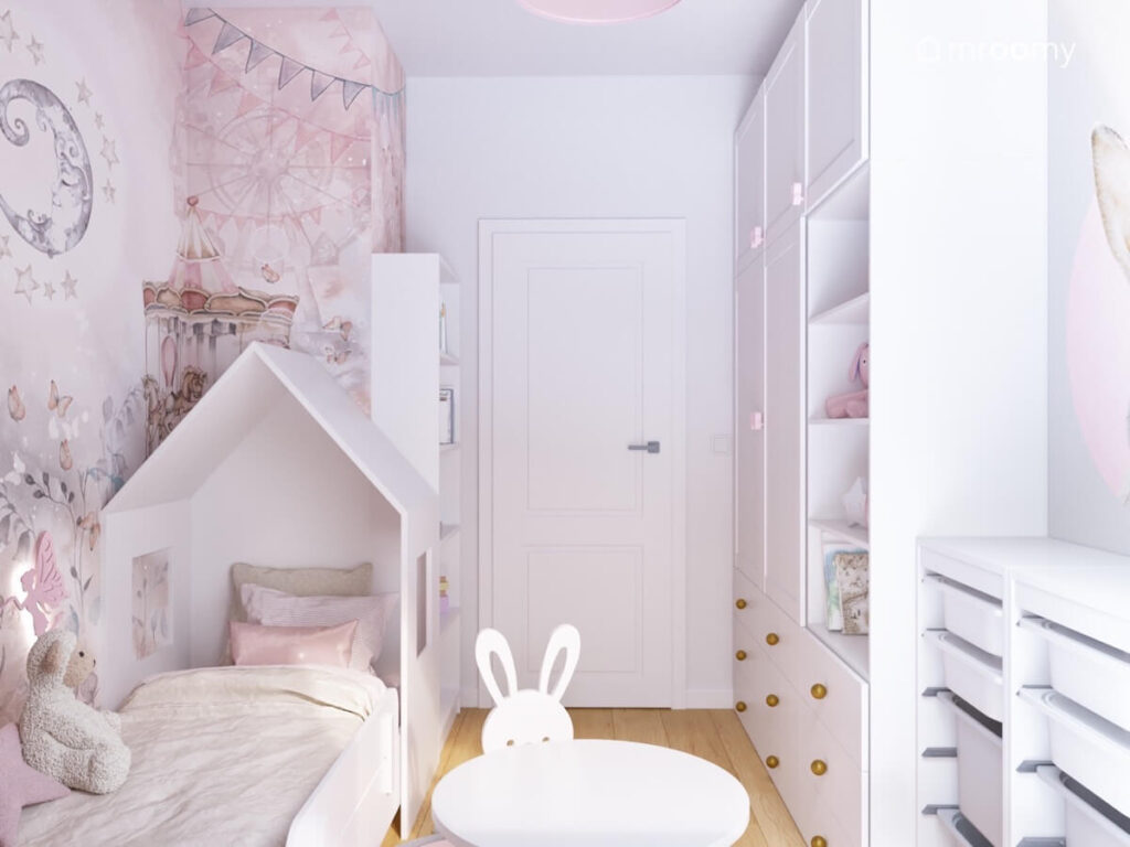 Białe łóżko w kształcie domku oraz inne białe meble w jasnym pokoju dla małej dziewczynki udekorowanym bajeczną tapetą z karuzelą