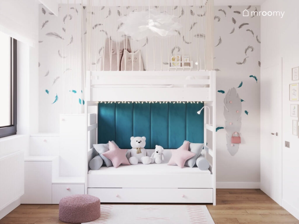 Biała antresola w pokoju dla dziewczynki na dole uzupełniona niebieskimi panelami ściennymi a na ścianie tapeta w pióra i wieszak również w formie pióra