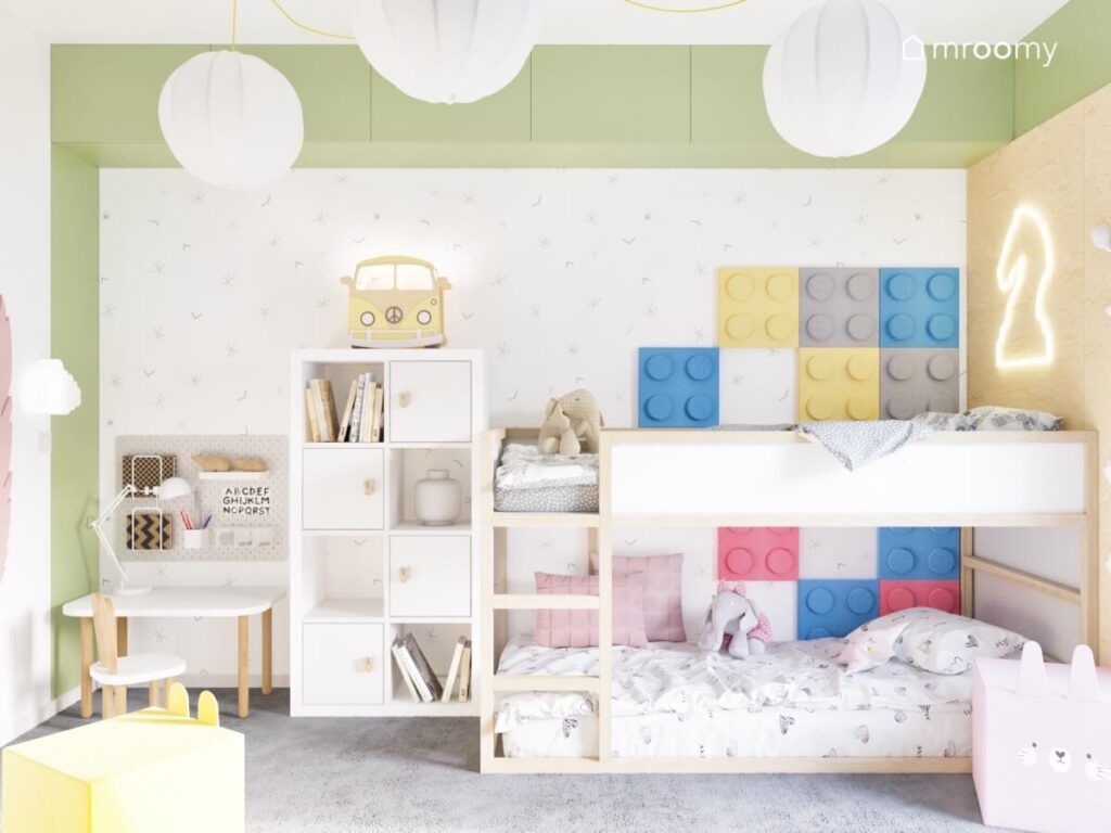 Strefa spania w pokoju dla rodzeństwa a w niej biało drewniane meble kolorowe panele ścienne w kształcie klocków minimalistyczna tapeta oraz lampka van