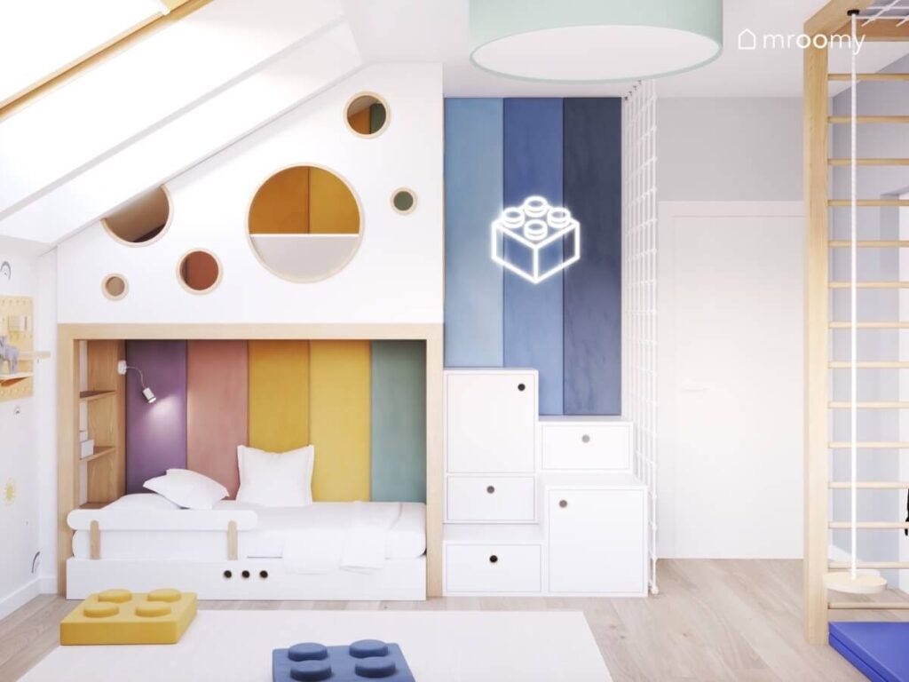 Biało drewniana antresola w pokoju dla chłopca uzupełniona miękkimi panelami w tęczowych kolorach oraz ledonem w kształcie klocka