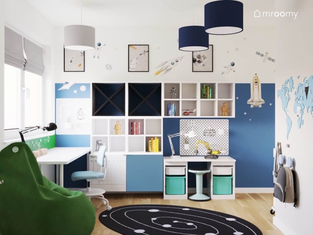 Biało niebieski pokój dla chłopca z kosmicznymi motywami licznymi szafkami ściennymi i stolikiem do zabawy