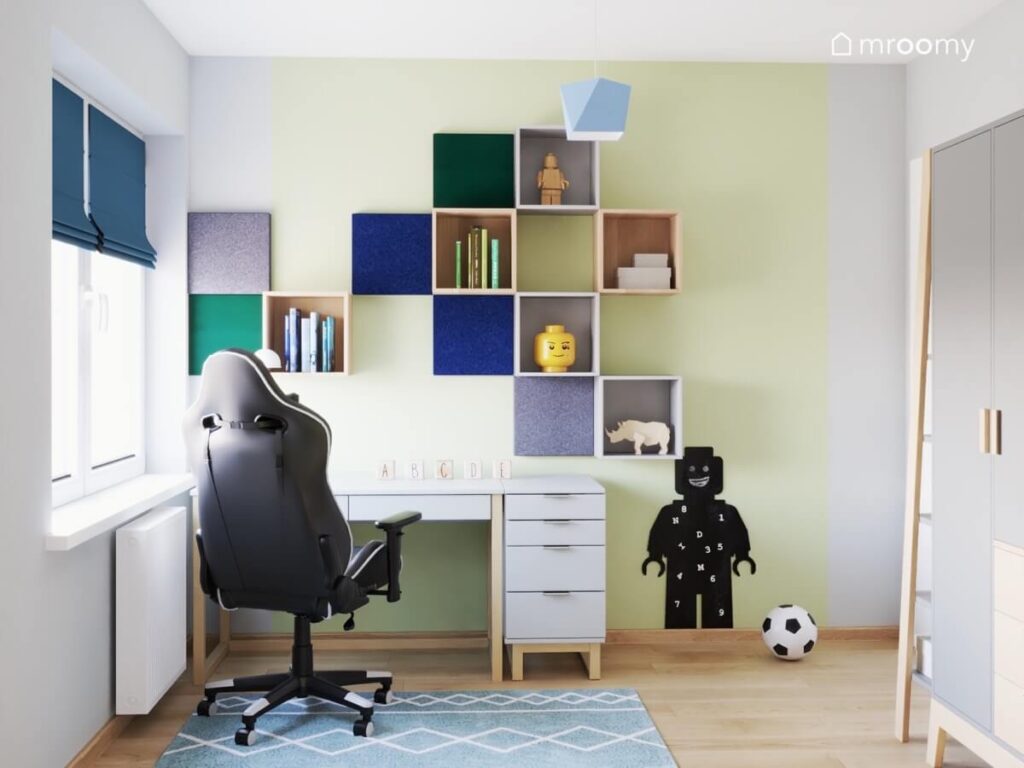 Strefa nauki w zielono szarym pokoju dla chłopca a w niej biurko z kontenerkiem szafki ścienne i kwadratowe panele oraz tablica kredowa w kształcie ludzika Lego