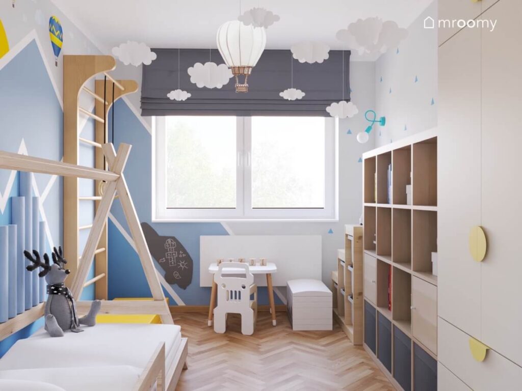 Jasny pokój dla chłopca a w nim drewniany regał i drabinka gimnastyczna i łóżko domek a u sufitu balony oraz chmurki