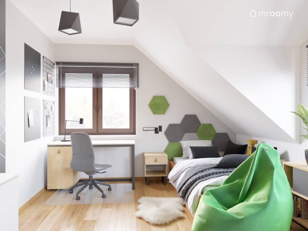 Szaro biały poddaszowy pokój dla chłopca w wieku szkolnym a w nim drewniane meble miękki dywanik i zielona pufa