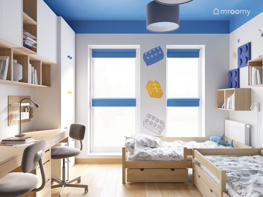 Biało szaro niebieski pokój dwóch chłopców a w nim drewniane i białe meble oraz dodatki w kształcie klocków Lego