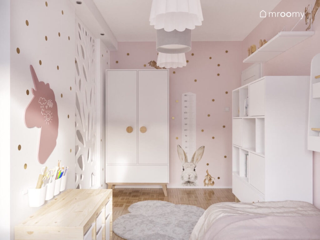 Biało różowy pokój dla dziewczynek z białą szafą i dużym regałem a na ścianie miarka wzrostu z królikiem tablica kredowa w kształcie jednorożca oraz kropki