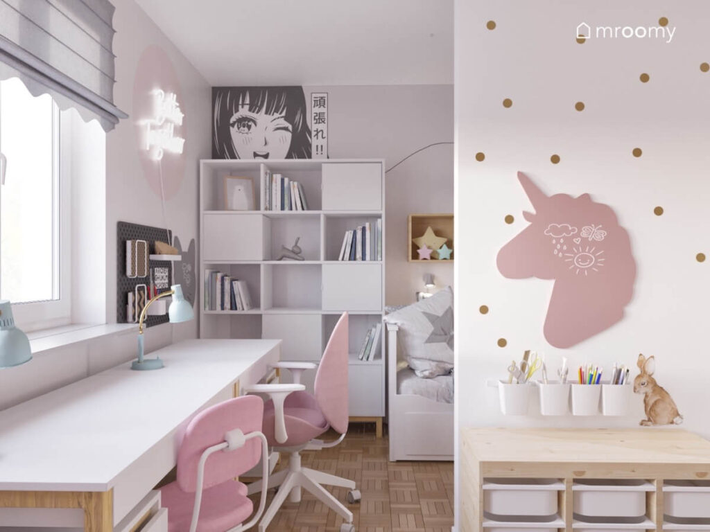 Strefa nauki w biało szarym pokoju dla dziewczynek a w niej długie biurko z różowymi krzesłami oraz duży regał a na ścianie tablica kredowa w kształcie jednorożca
