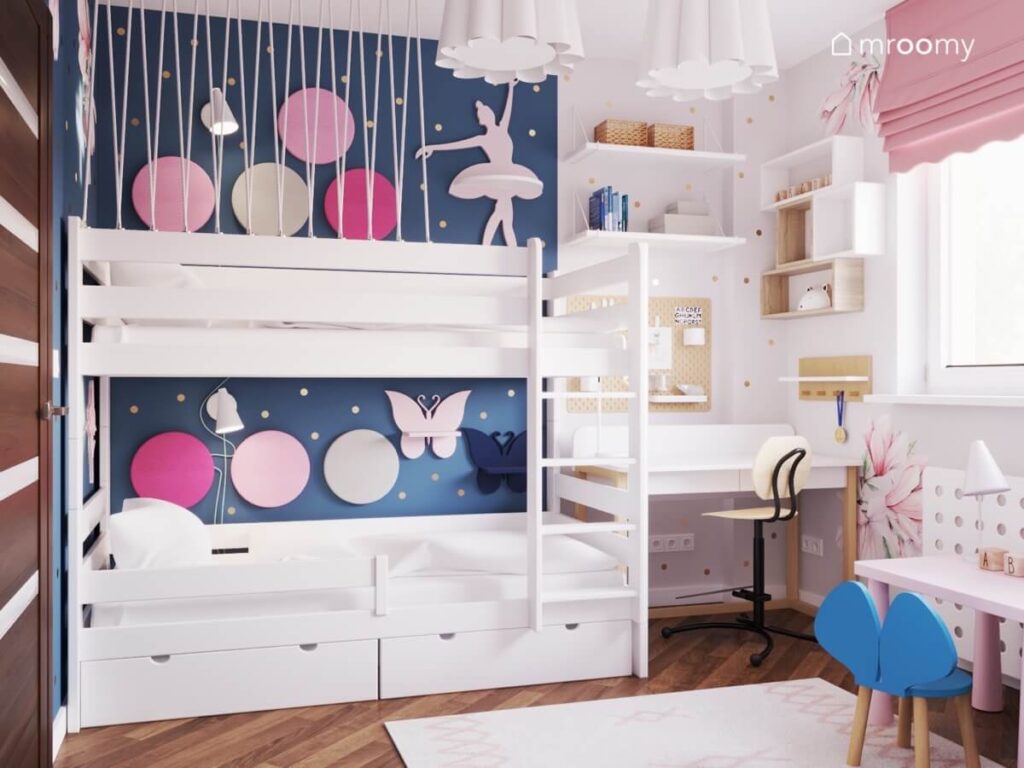 Białe łóżko piętrowe w pokoju dwóch dziewczynek uzupełnione okrągłymi panelami w różnych odcieniach a obok strefa nauki z półkami i organizerem