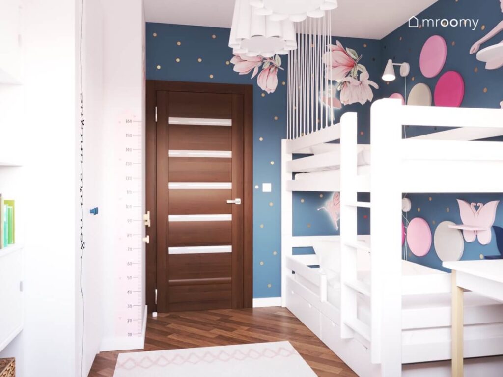 Granatowa strefa spania w pokoju dwóch dziewczynek a w niej białe łóżko piętrowe naklejki kwiaty oraz okrągłe panele na ścianie