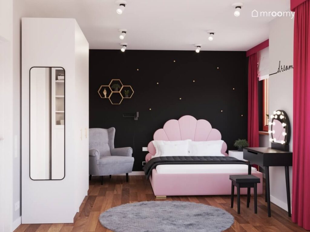 Strefa spania w pokoju nastolatki a w niej różowe tapicerowane łóżko z ozdobnym wezgłowiem szary fotel a na czarnej ścianie złote akcenty