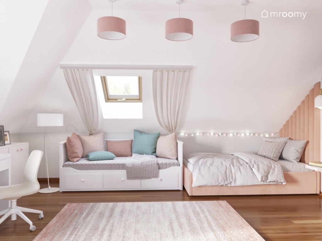 Brzoskwiniowe tapicerowane łóżko oświetlone girlandą świetlną a obok kanapa z licznymi poduszkami w białym poddaszowym pokoju nastolatki