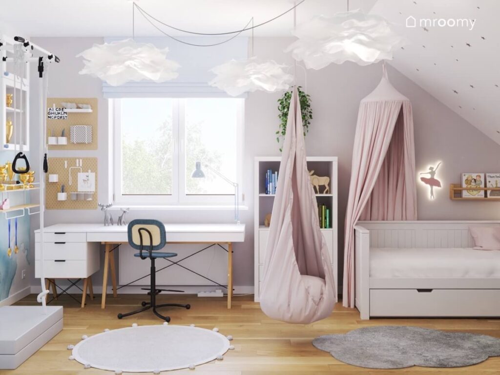 Poddaszowy pokój dla dziewczynki w wieku szkolnym a w nim strefa nauki łóżko uzupełnione baldachimem wiszący fotel kokon a na suficie ozdobne lampy w papierowych kloszach