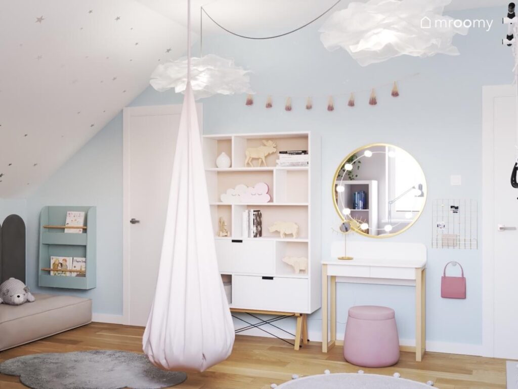 Niebiesko biały pokój dla dziewczynki ze skosem ozdobionym gwiazdkami oraz dużym regałem z szufladami toaletką i fotelem kokonem oraz girlandą pomponów na ścianie