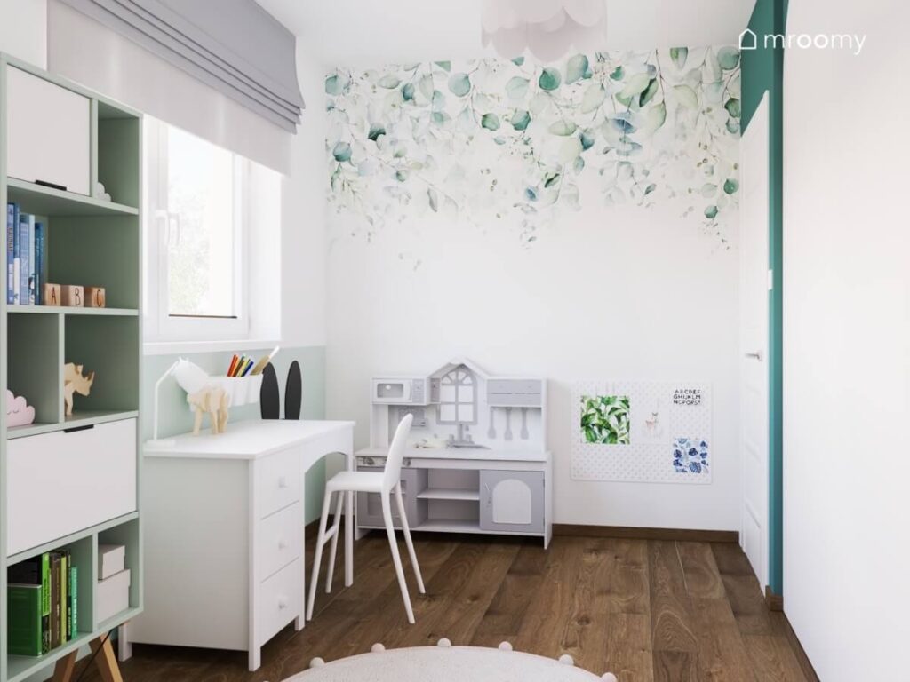 Białe biurko z prostym krzesłem kuchnia dla dzieci organizer a na ścianie tapeta w liście w jasnym pokoju małej dziewczynki