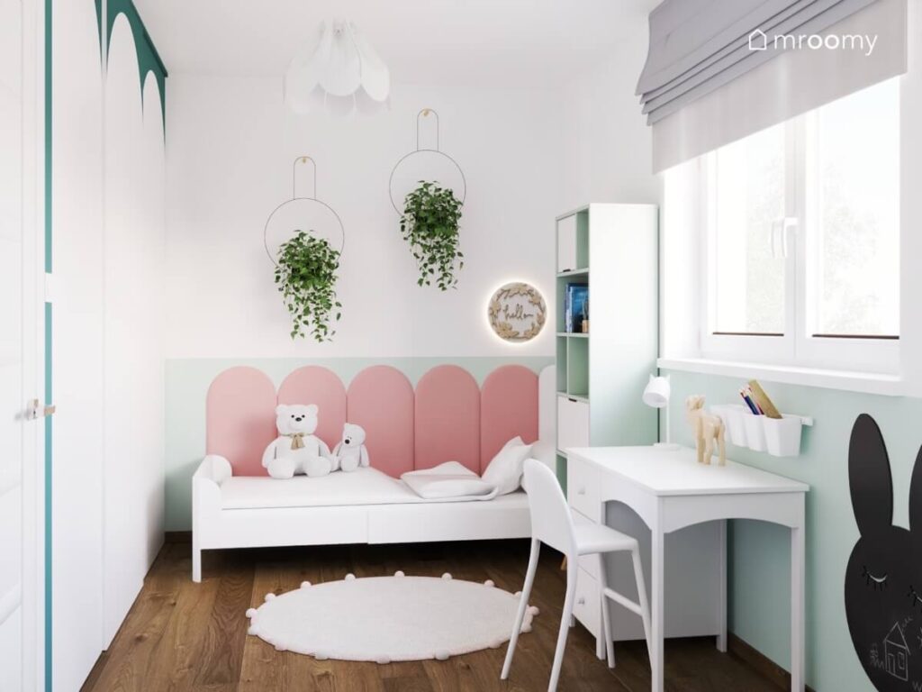 Białe łóżko uzupełnione różowymi panelami ściennymi nad nim ozdobne kwietniki oraz lampka nocna a na podłodze dywan w pokoju małej dziewczynki