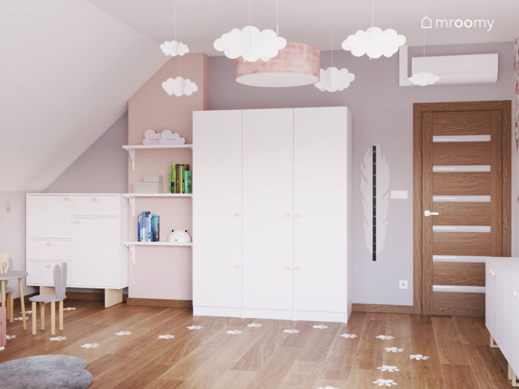 Biało szary poddaszowy pokój dla dziewczynki z trzydrzwiową szafą półkami ściennymi oraz papierowymi chmurkami u sufitu i śladami łapek na podłodze