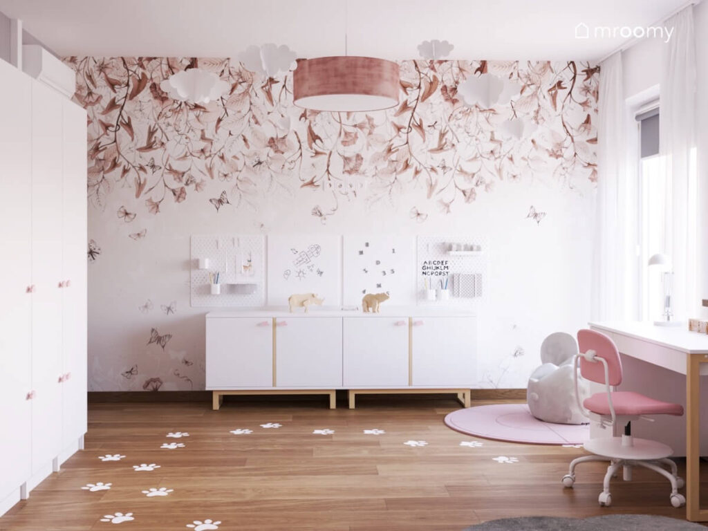 Ściana w pokoju kilkuletniej dziewczynki a na niej tapeta w kwiaty i liście organizery i białe szafki