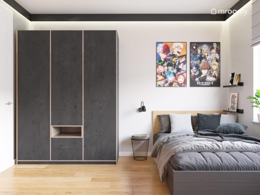 Duża czarna szafa z drewnianymi elementami w pokoju nastolatki a obok duże łóżko nad którym wiszą plakaty z anime