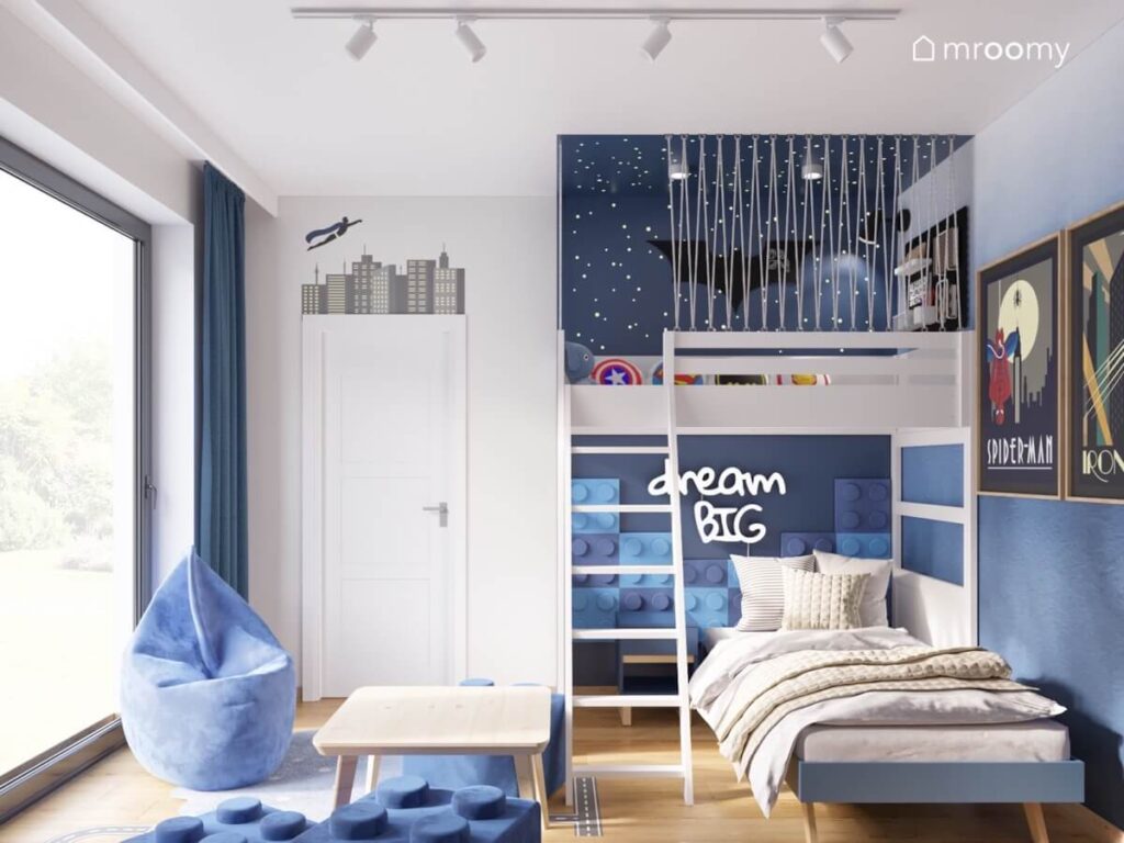 Biała antresola w pokoju dla chłopca z miejscem do zabawy a pod spodem niebieskie łóżko a na ścianach motywy superbohaterskie