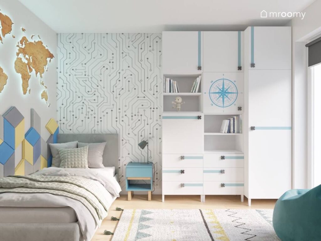 Białe meble modułowe z gałkami w kształcie iksów niebieski stolik nocny i szare łóżko a na ścianie tapeta w cybernetyczny wzór w pokoju chłopca