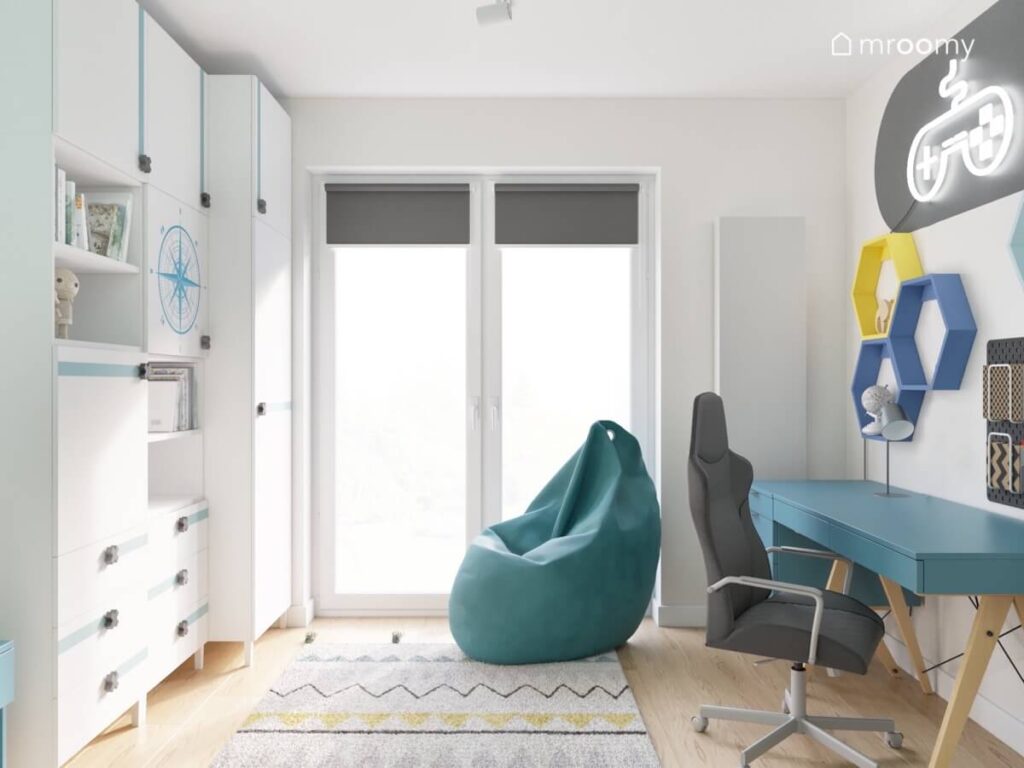 Jasnoszary pokój dla chłopca w wieku szkolnym a w nim niebieskie biurko z wygodnym fotelem duża pufa i wzorzysty dywan
