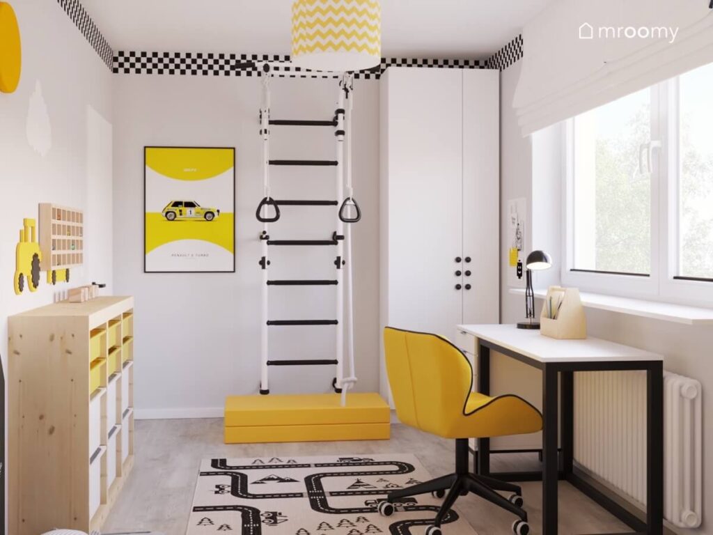 Biały pokój dla chłopca z wysoką białą szafą czarno białą drabinką gimnastyczną żółtym materacem oraz paskiem w szachownicę u sufitu