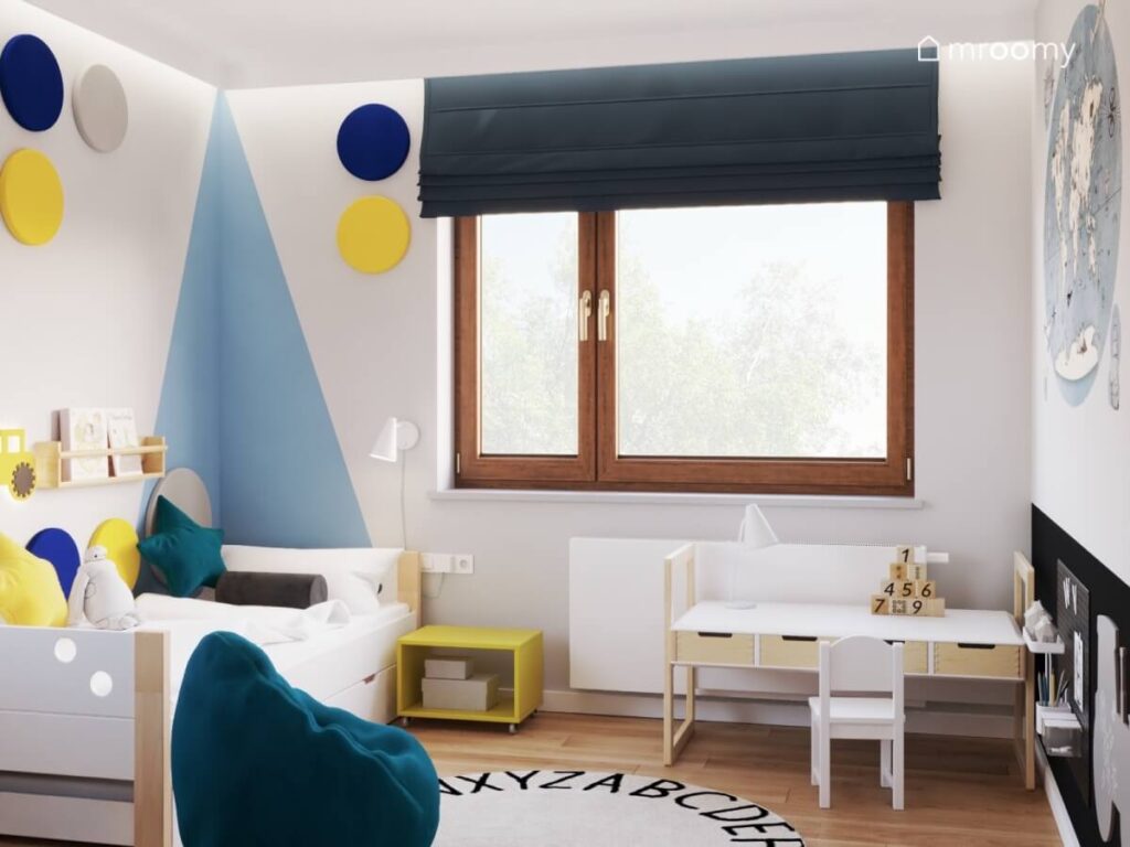 Biały pokój dla chłopca z błękitnym fragmentem ściany biało drewnianymi meblami ciemnoniebieską pufą oraz kolorowymi panelami ściennymi