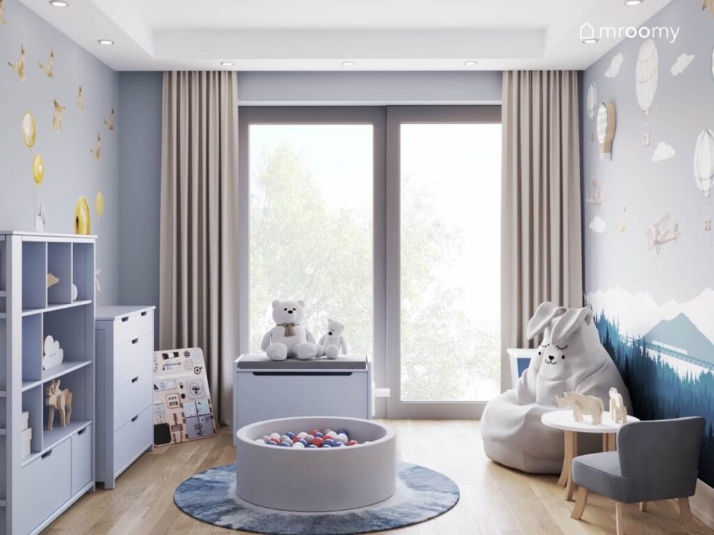 Pokój dla małego chłopca a w nim szaroniebieskie meble basen z kulkami skrzynia na zabawki oraz pufa królik