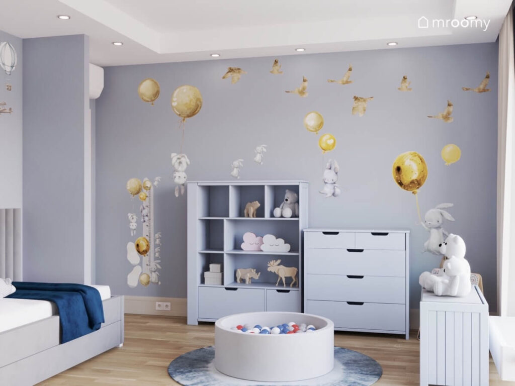 Szaroniebieski pokój dla małego chłopca a w nim meble w podobnym kolorze i basen z kulkami oraz naklejki ścienne króliki ptaki i złote balony