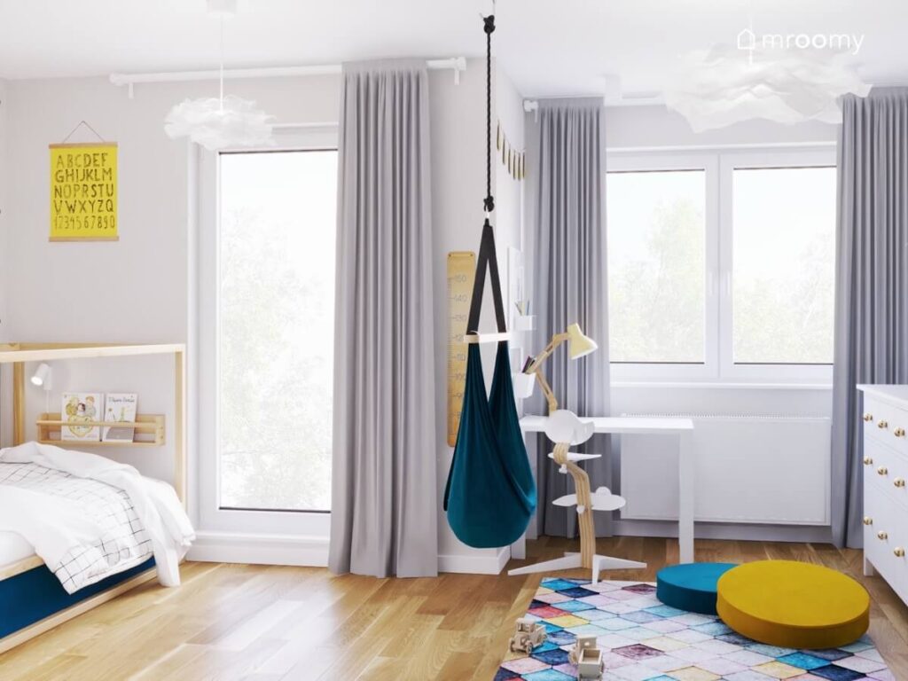 Biały pokój dla chłopca z białym biurkiem fotelem wiszącym oraz kolorowym dywanem i pufkami