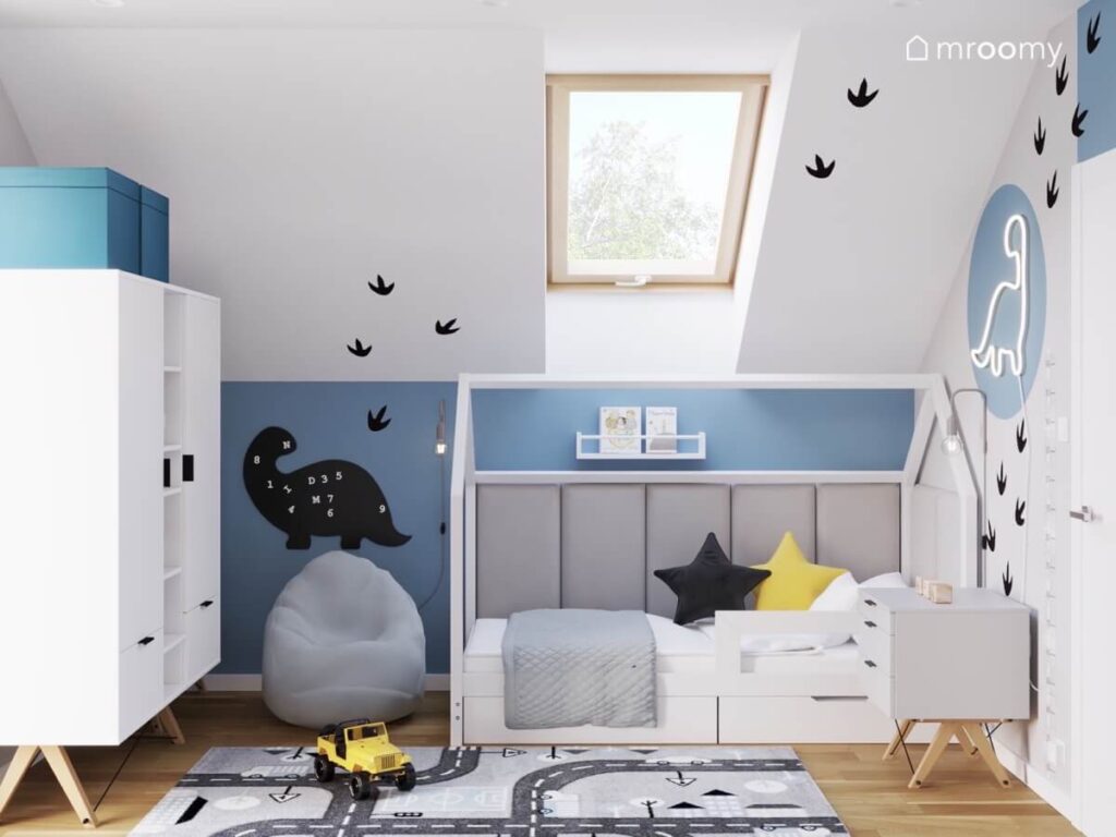 Biało szaro niebieski pokój dla chłopca z białą szafą łóżkiem domkiem pufą oraz tablicą kredową w kształcie dinozaura