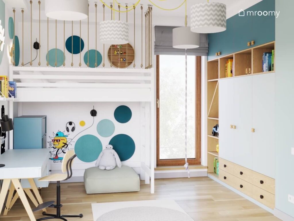 Biała antresola uzupełniona niebieskimi panelami ściennymi oraz biała szafa z drewnianymi półkami i szufladami a na środku wisząca lina w pokoju chłopca