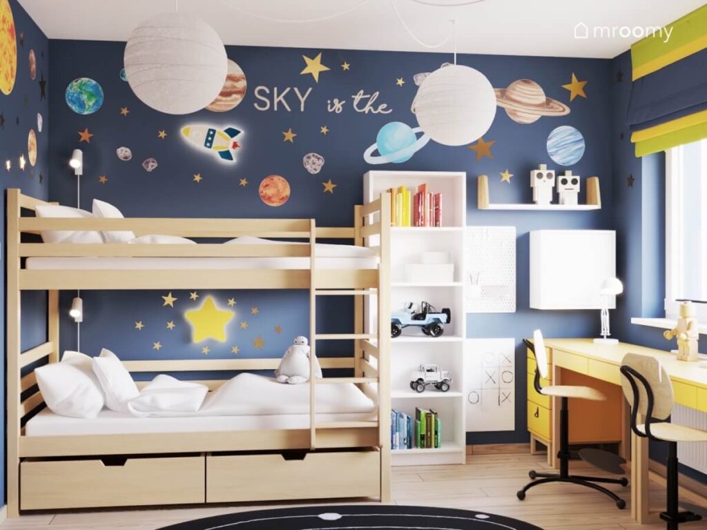 Drewniane łóżko piętrowe obok biały regał i organizery a na ścianie kosmiczne naklejki i lampki rakieta i gwiazda