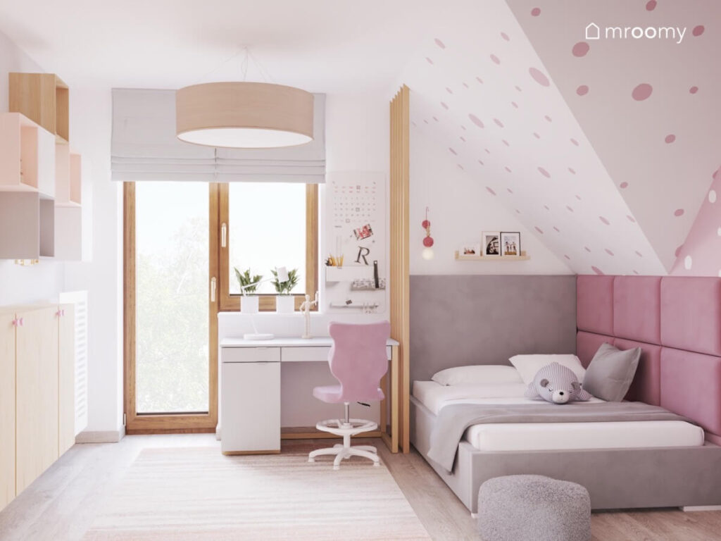 Jasny poddaszowy pokój dla dziewczynki z białym biurkiem z różowym krzesłem i szarym łóżkiem uzupełnionym różowymi panelami ściennymi