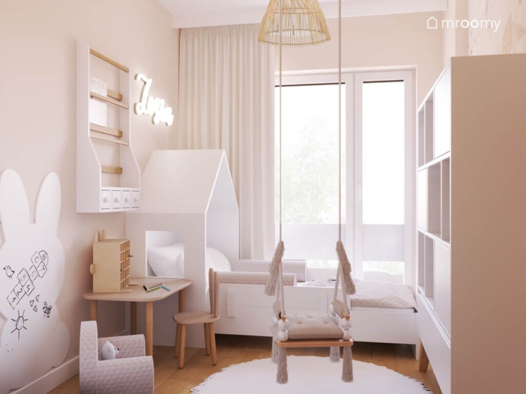 Przytulny pokój dla dziewczynki z białym łóżkiem domkiem huśtawką wiszącą oraz biblioteczką i małym stolikiem