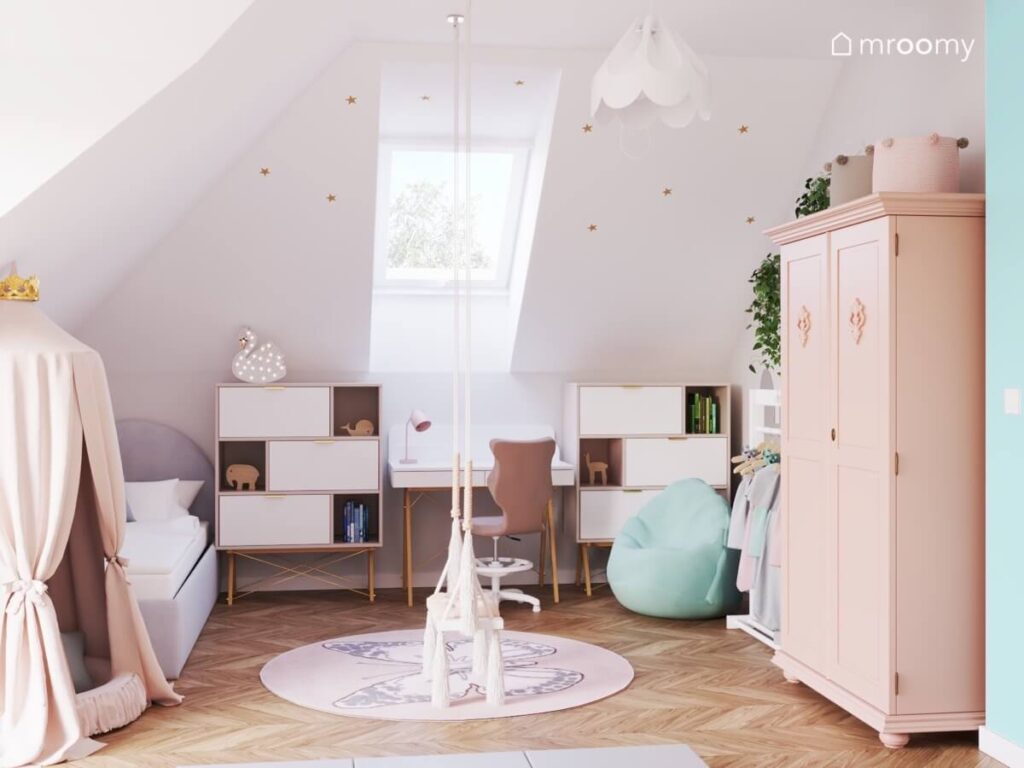 Biały poddaszowy pokój dla dziewczynki z szarym łóżkiem jasnymi meblami miętową pufą oraz huśtawką z frędzlami i dywanem z motylem