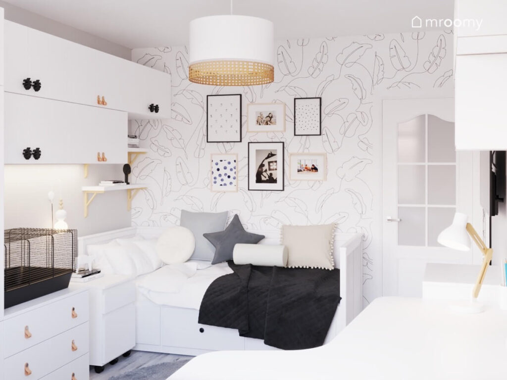 Strefa spania w pokoju nastolatki z białym łóżkiem z szufladami oraz obrazkami i tapetą w liście na ścianie