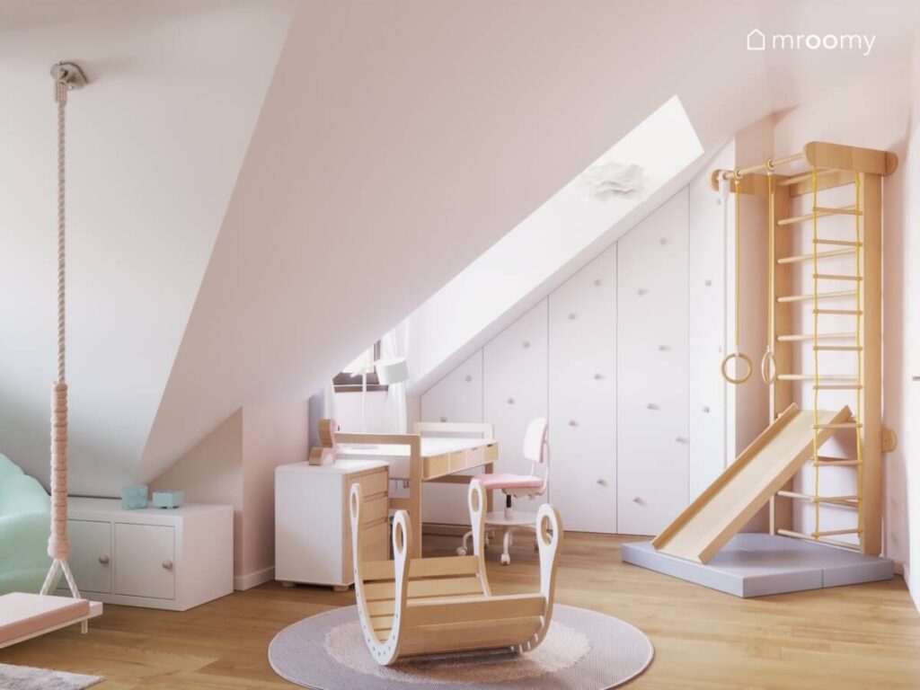 Biały pokój dla małej dziewczynki na poddaszu z drewnianym bujakiem drabinką gimnastyczną ze zjeżdżalnią oraz biurkiem