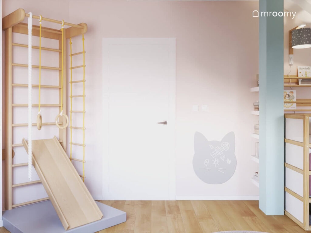 Drabinka gimnastyczna ze zjeżdżalnią oraz materacem a także tablica kredowa w kształcie kota w jasnym pokoju dziewczynki