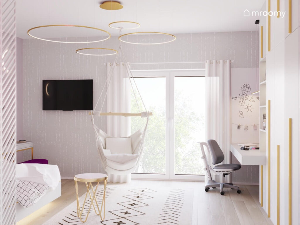 Fotel wiszący dywan z geometrycznym wzorem na ścianie szara tapeta a na suficie złote lampy w kształcie pierścieni w pokoju dla dziewczynki