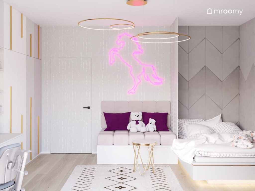 Szary pokój dla dziewczynki a w nim różowe siedzisko i ledon w kształcie konia a obok łóżko i szare geometryczne panele na ścianie a na suficie złote lampy
