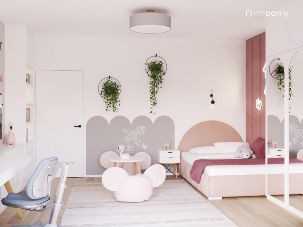 Biały pokój dla dziewczynki z różowym łóżkiem szarą powierzchnią kredową oraz kwietnikami na ścianie