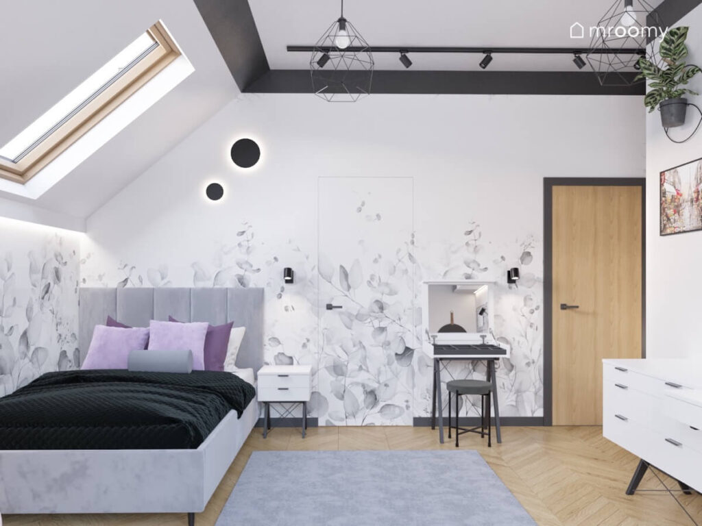 Biały poddaszowy pokój dla nastolatki z szarym tapicerowanym łóżkiem toaletką oraz tapetą w kwiaty