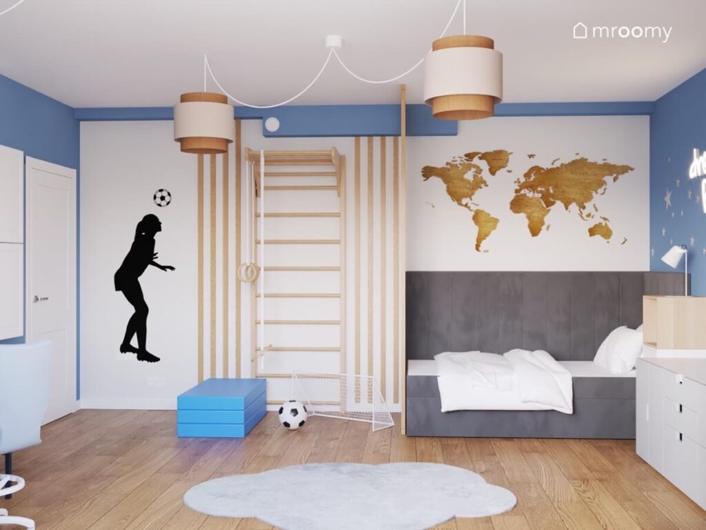 Biało niebieski pokój dla dziewczynki a w nim drewniana drabinka gimnastyczna szare łóżko tapicerowane mapa świata oraz naklejka piłkarka