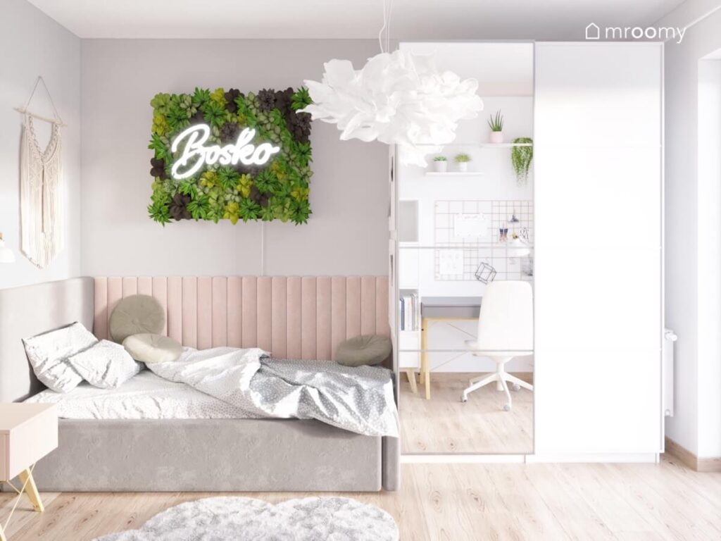 Szary pokój nastolatki a w nim szare łóżko uzupełnione różowymi panelami ściennymi obok biała szafa z lustrzanym frontem na ścianie rośliny a na suficie lampa w ozdobnym kloszu